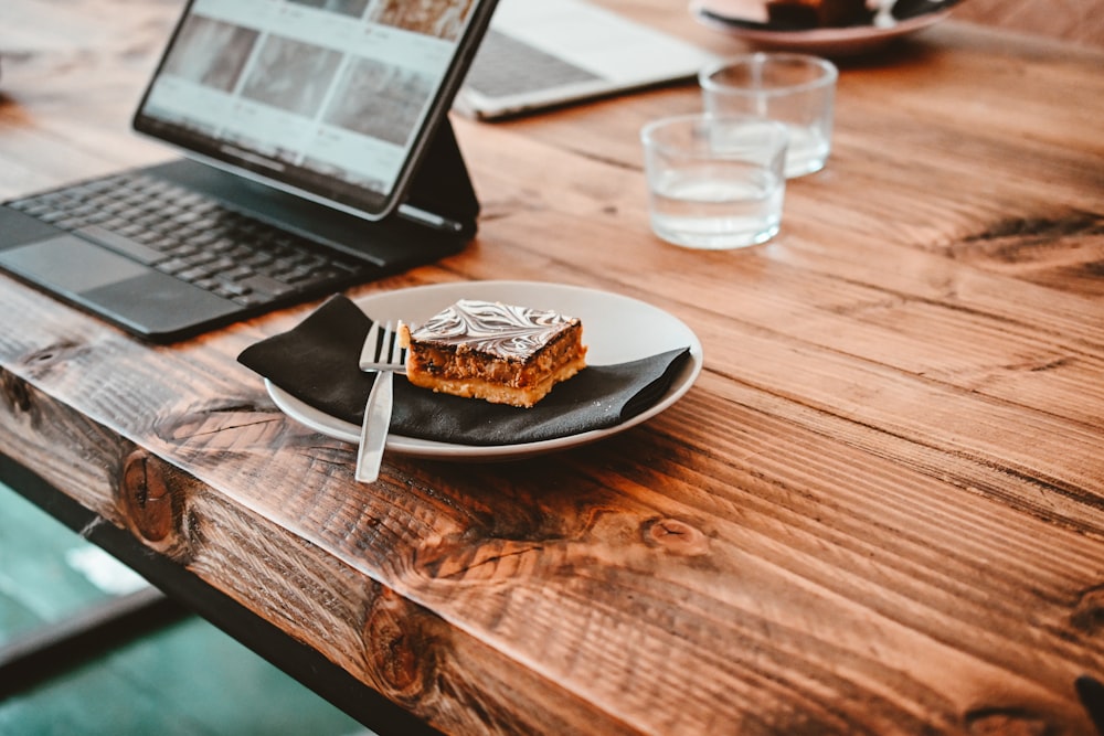 a plate with a piece of cake on it next to a laptop