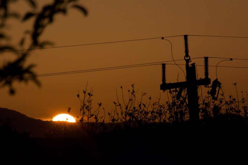 the sun is setting behind a telephone pole