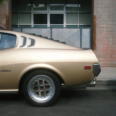 a tan car parked in front of a brick building