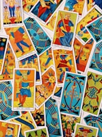 A colorful assortment of tarot cards is laid out, featuring a variety of illustrations, including figures, symbols, and mythical imagery. The cards are overlapping, each with vibrant colors and intricate designs, representing different suits and trumps within the tarot deck.