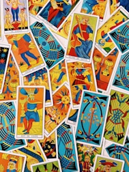A colorful assortment of tarot cards is laid out, featuring a variety of illustrations, including figures, symbols, and mythical imagery. The cards are overlapping, each with vibrant colors and intricate designs, representing different suits and trumps within the tarot deck.