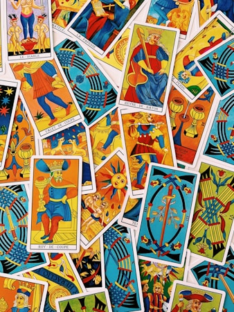 A colorful assortment of tarot cards is laid out, featuring a variety of illustrations, including figures, symbols, and mythical imagery. The cards are overlapping, each with vibrant colors and intricate designs, representing different suits and trumps within the tarot deck.