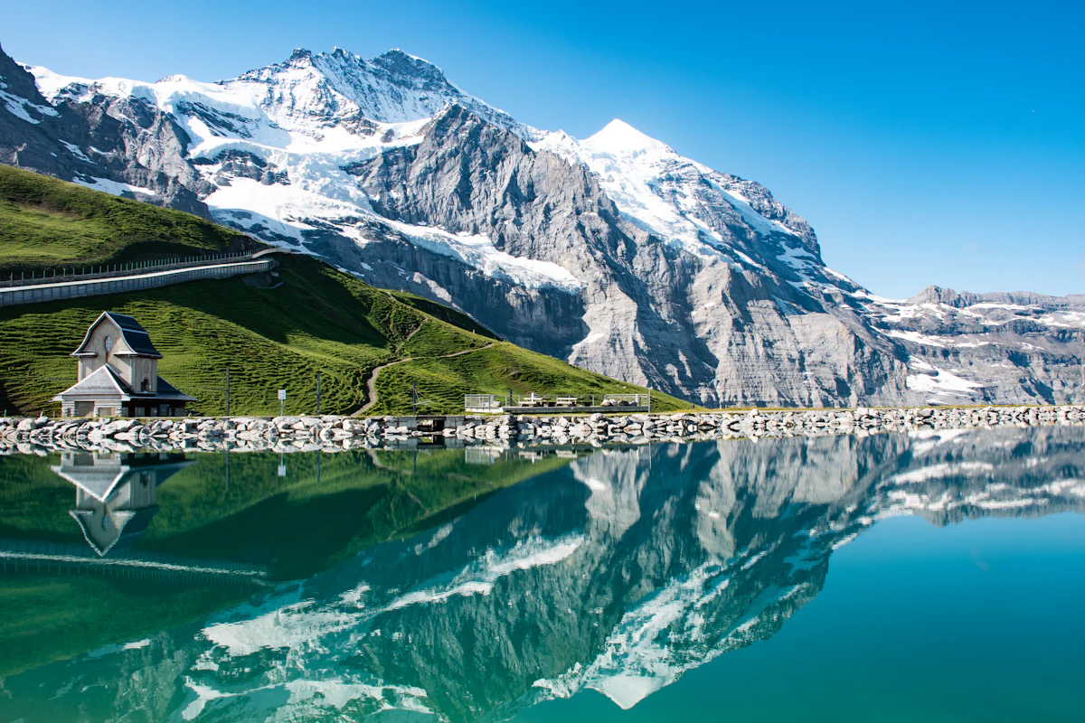 A snowy peak and a small stone building reflected in a calm alpine lake near Grindelwald