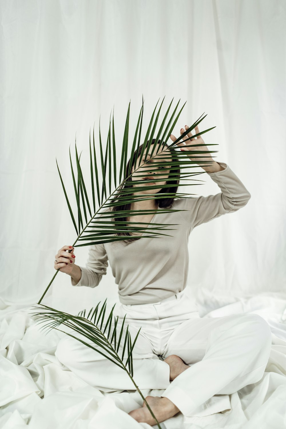 a woman sitting on a bed holding a palm leaf