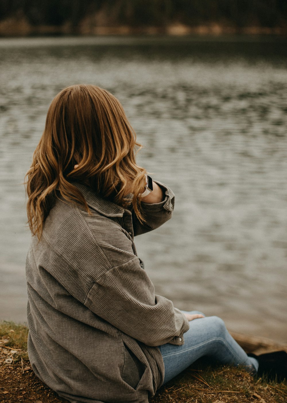 a woman sitting on the shore of a lake