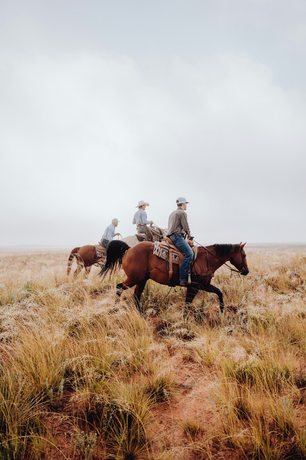 a group of people riding horses through a dry grass field