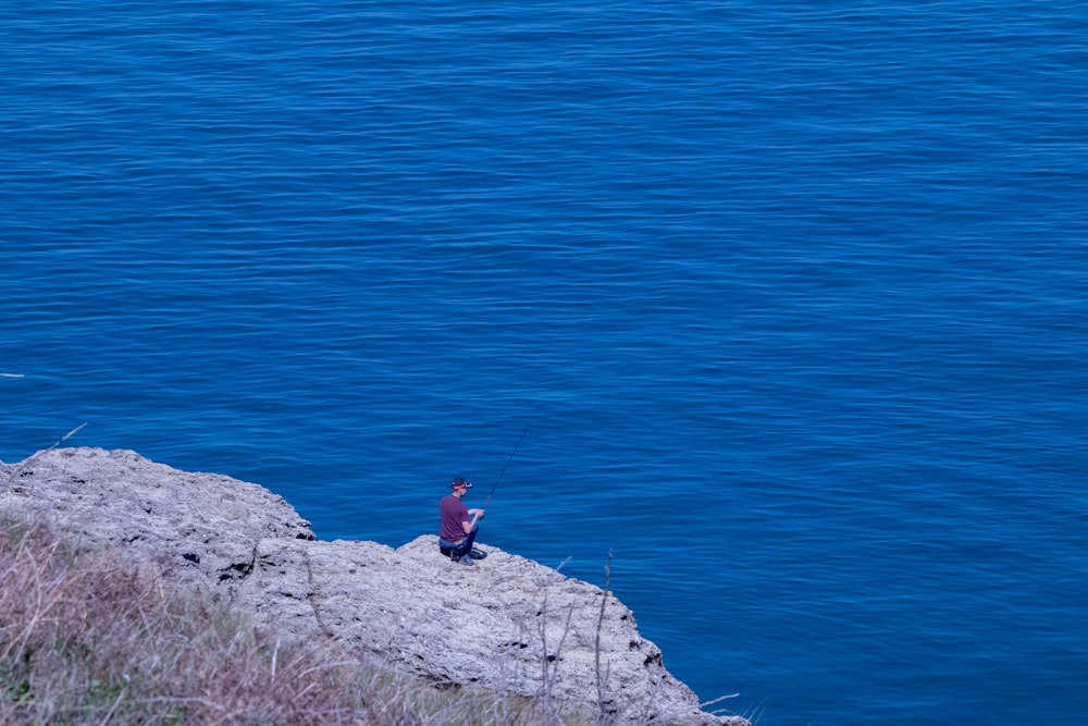 a man sitting on top of a cliff next to a body of water