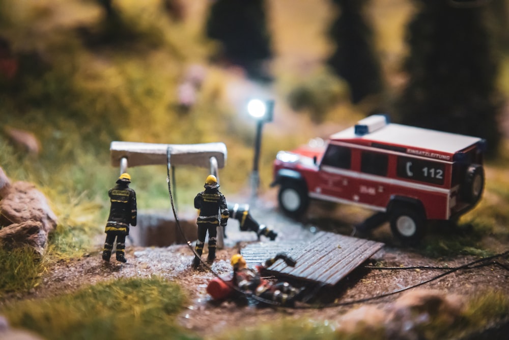 a couple of toy firemen standing next to a fire truck