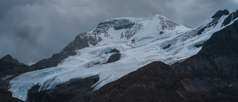 a mountain covered in snow under a cloudy sky