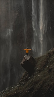 a person standing on a rock in front of a waterfall