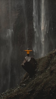 a person standing on a rock in front of a waterfall