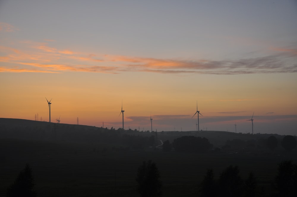 the sun is setting over a field of wind mills