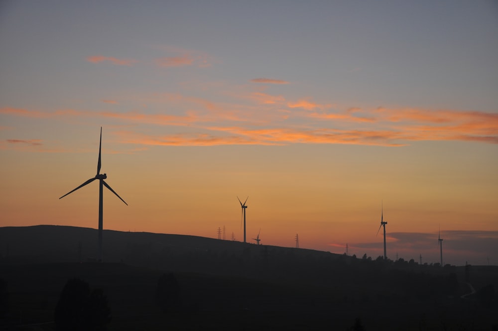 a group of windmills on a hill at sunset