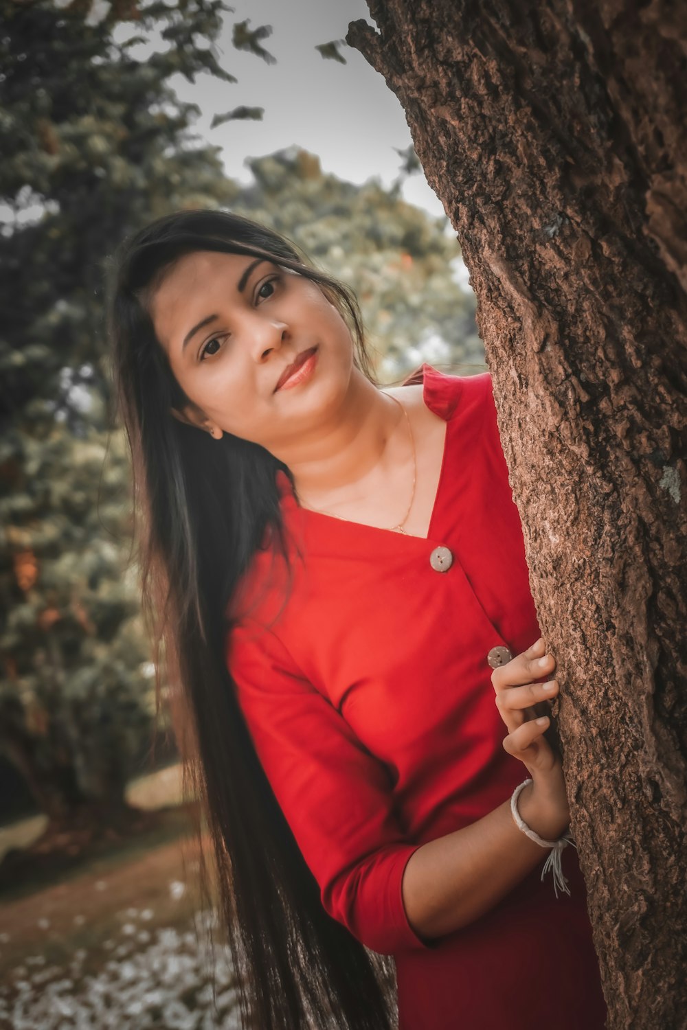 a woman in a red dress leaning against a tree