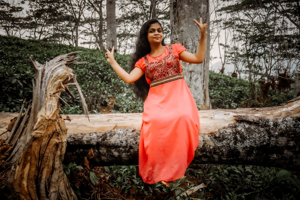 a woman in an orange dress standing on a log