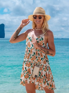 A sunlit beach scene with a woman carrying a colorful Beachcraft tote bag, wearing a breezy summer dress.