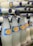A collection of glass bottles filled with a white liquid, arranged in a staggered manner. The bottles feature a blue and yellow label with text and are capped with blue metal lids.