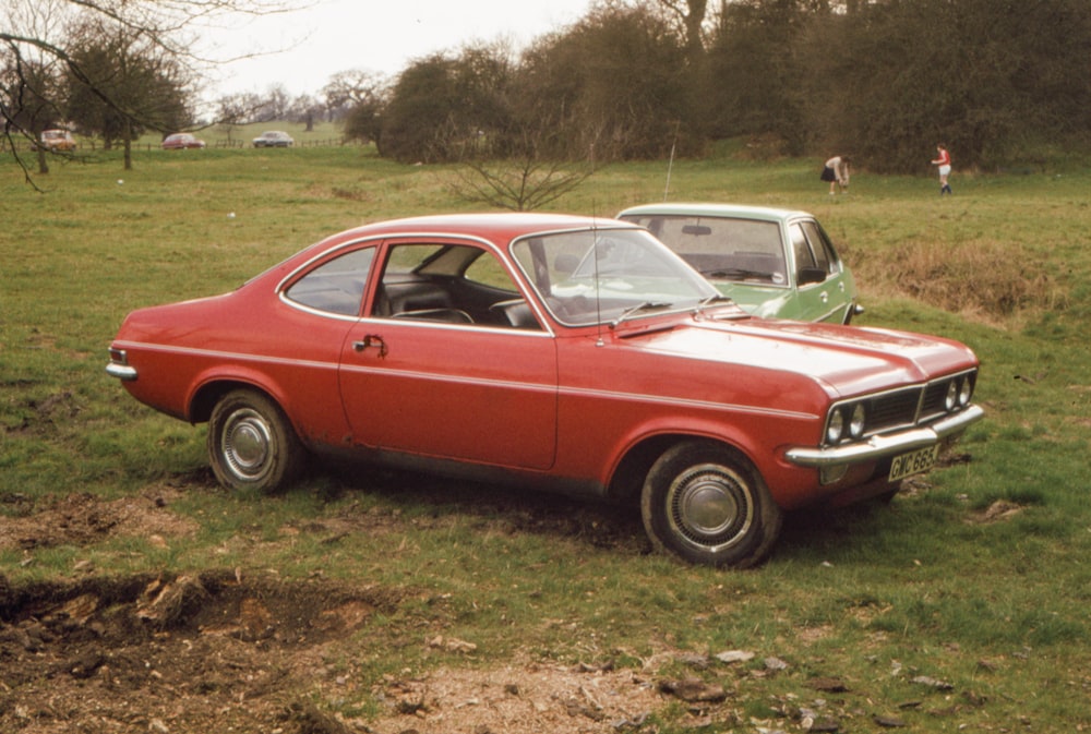 a red car parked in a field next to a green car