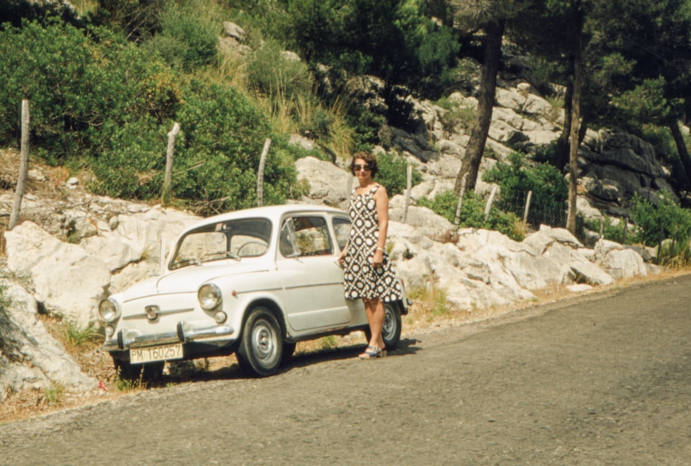a woman standing next to a white car on the side of a road