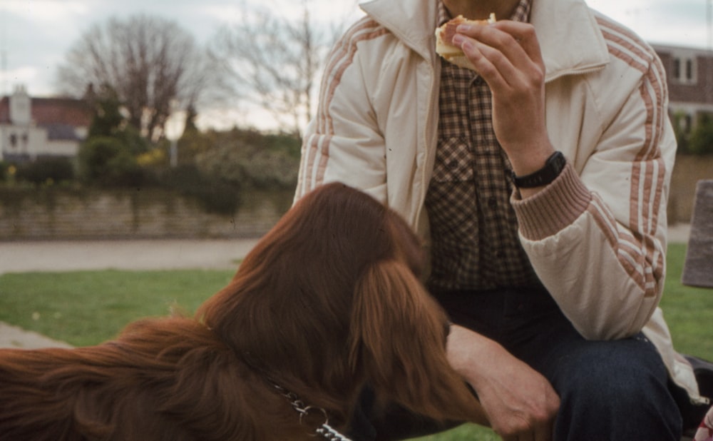 a man sitting on a bench eating a piece of food next to a dog