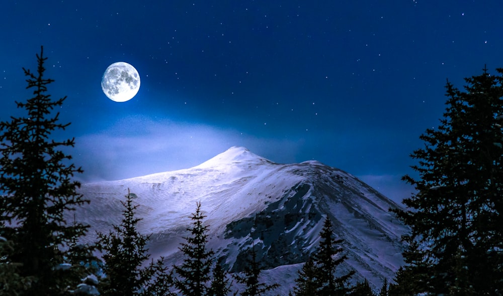 a full moon rises over a snowy mountain