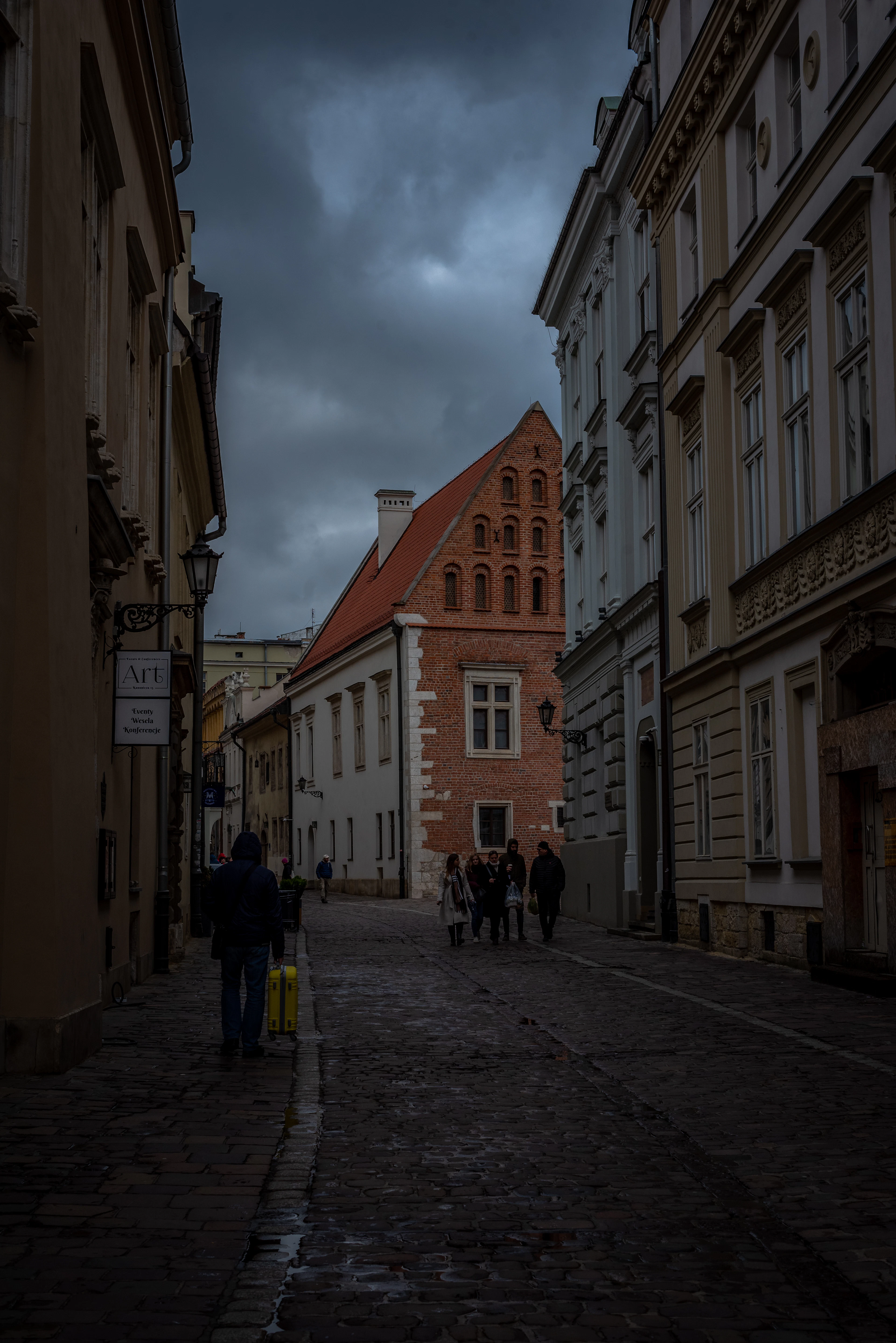 A cobblestone old-town street with a lantern-lit facade under dramatic storm clouds.