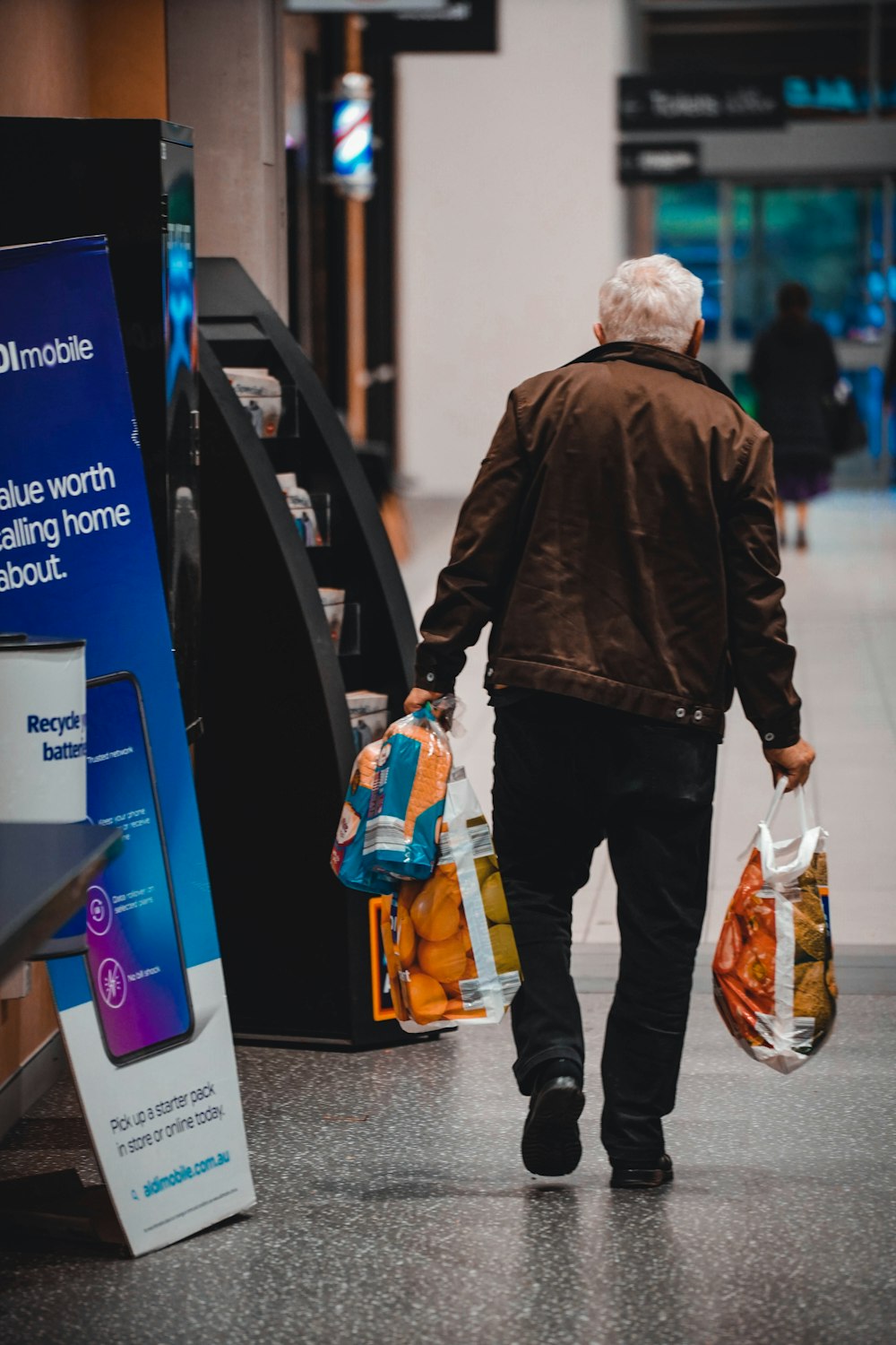 a man walking down a hallway carrying bags of oranges