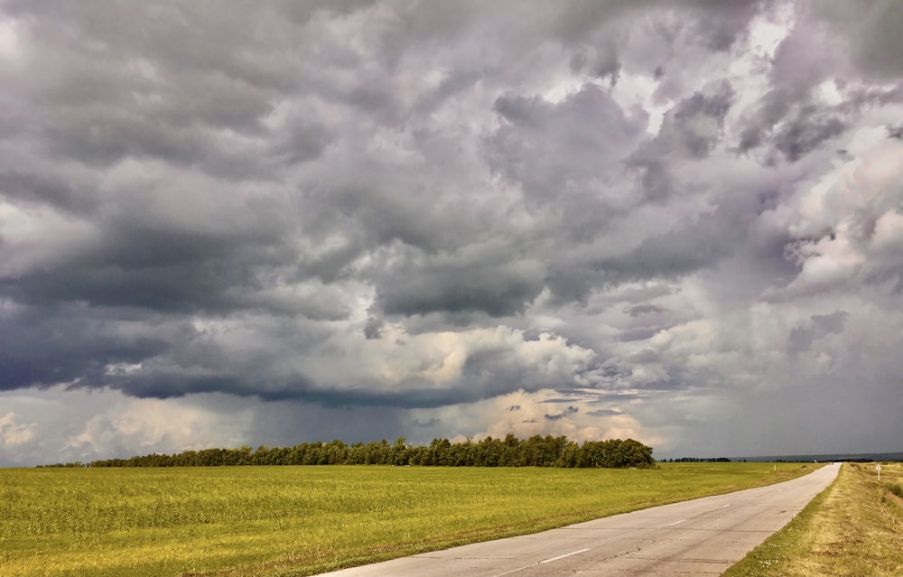 an empty road in a field under a cloudy sky