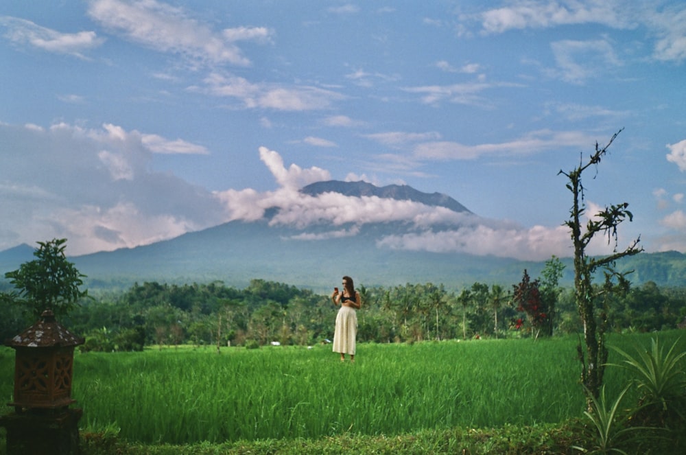 a woman standing in a field with a mountain in the background