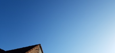 A section of a roof is visible in the lower part of the image against a clear blue sky. The roof is composed of tiles with a reddish-brown hue, partially illuminated by sunlight.