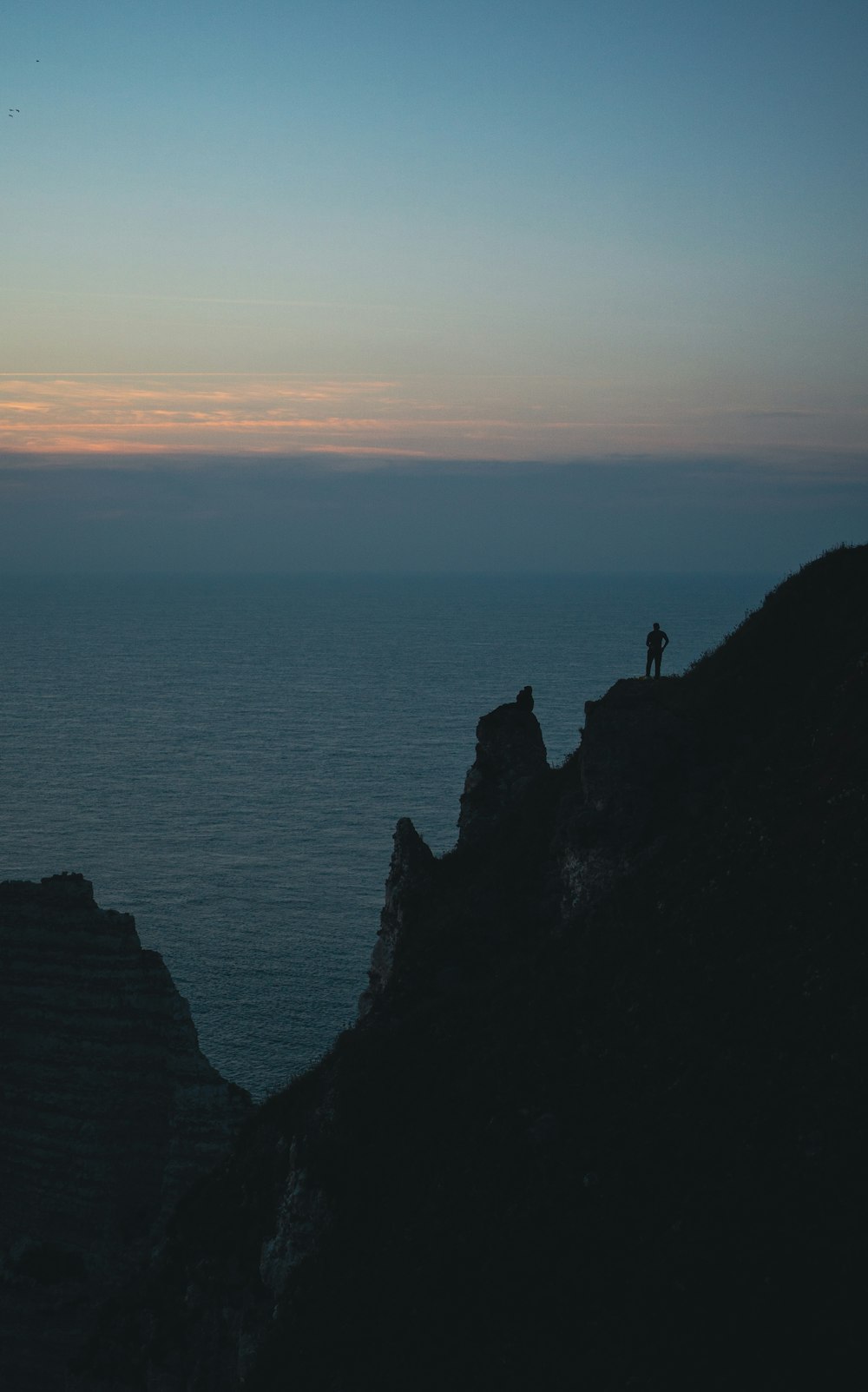 a person standing on top of a mountain next to the ocean