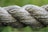 A close-up of a thick, twisted rope showcasing its fibrous texture and natural color variations. The greenish hue suggests it might be outdoors, possibly in a natural setting.