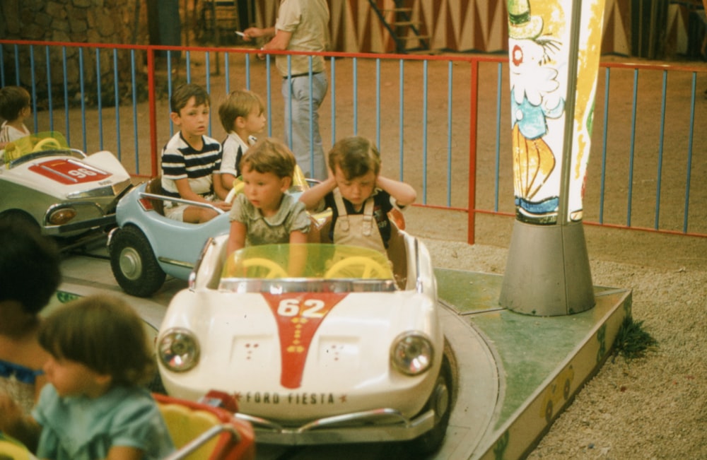a group of young children riding on top of a toy car