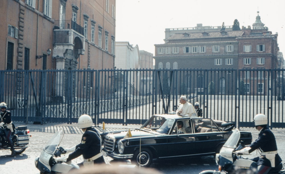 a group of men riding motorcycles next to a car