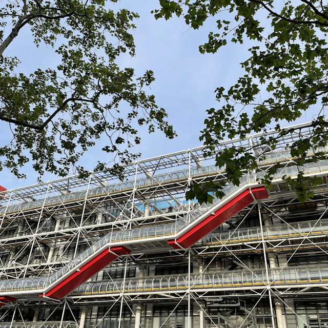 The Centre Pompidou in Paris seen between two trees, with its red external escalator tube running up the facade