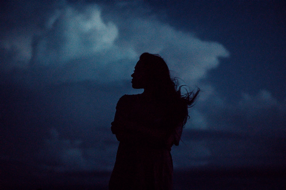 a woman standing in the dark with her hair blowing in the wind