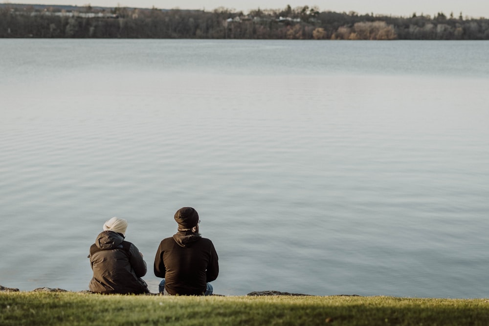 two people sitting on the shore of a lake