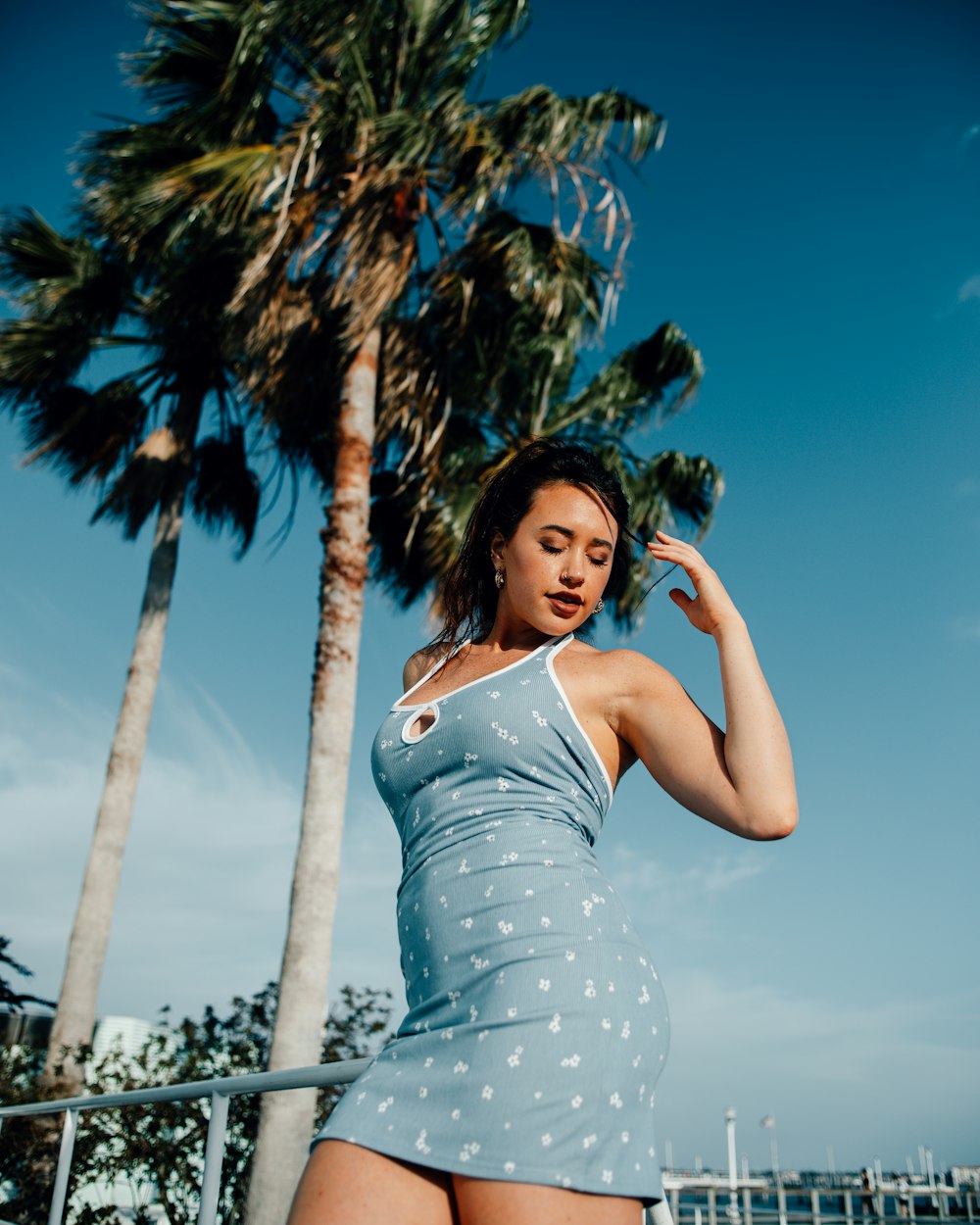 a woman in a blue dress standing next to a palm tree