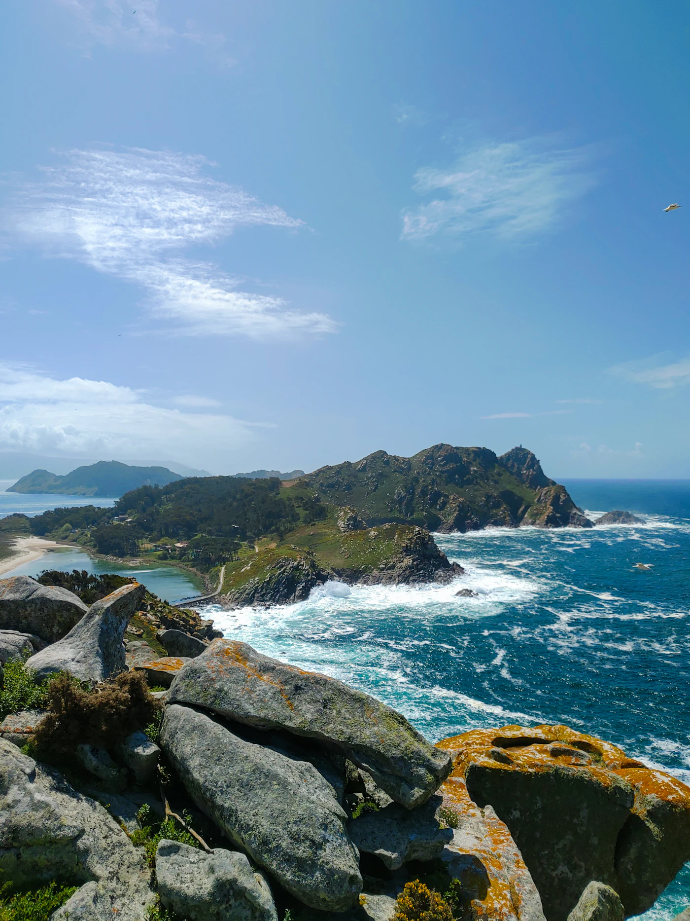 Rotsachtige kust van de Islas Cíes met golven, lagune en strand in de verte