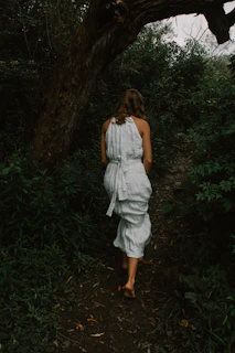A serene scene of a model walking barefoot on a forest path wearing organic cotton clothes.