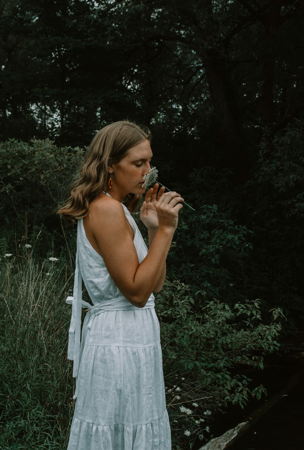 a woman in a white dress blowing a flower