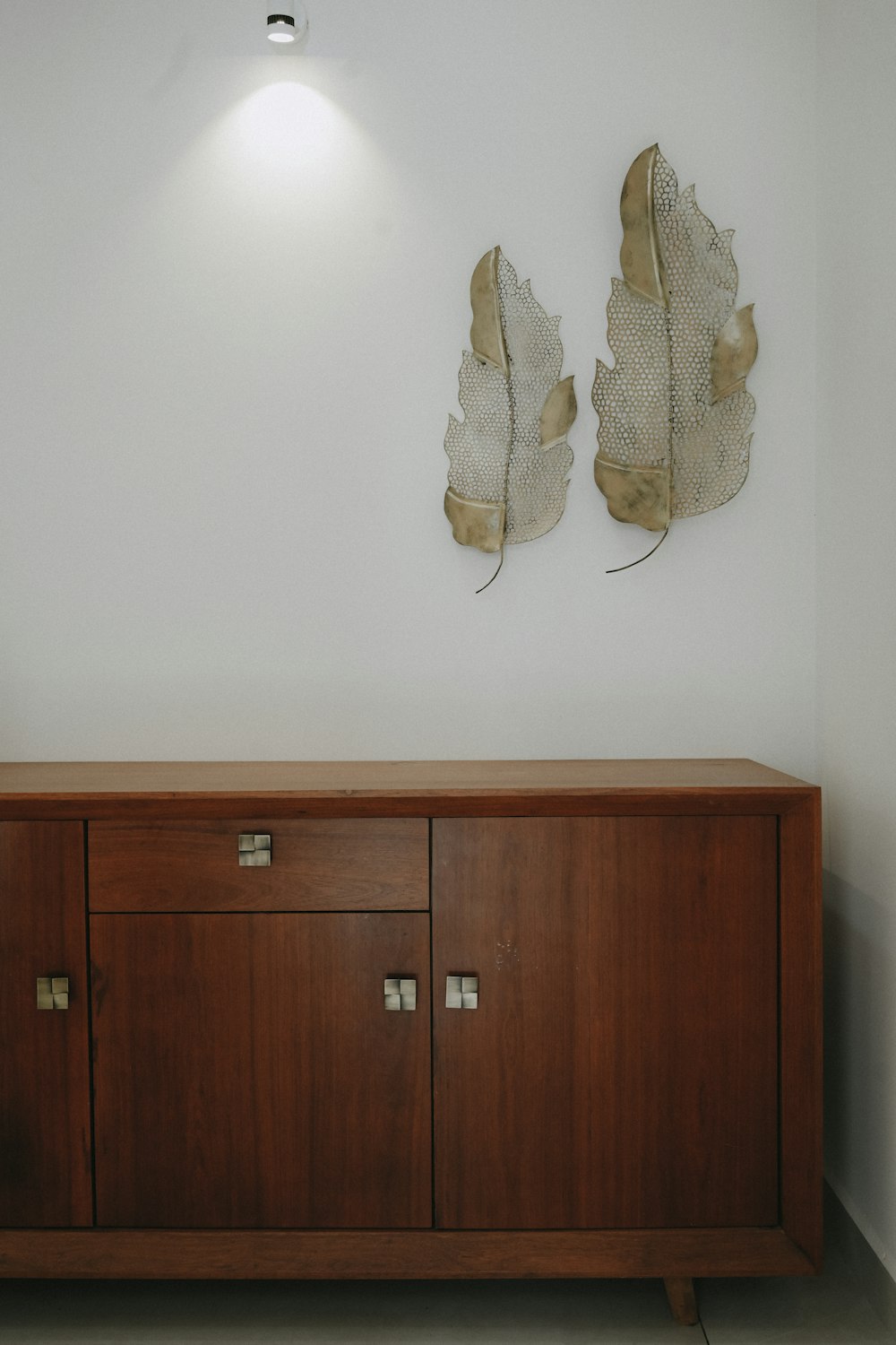 a wooden cabinet with two metal leaves on the wall