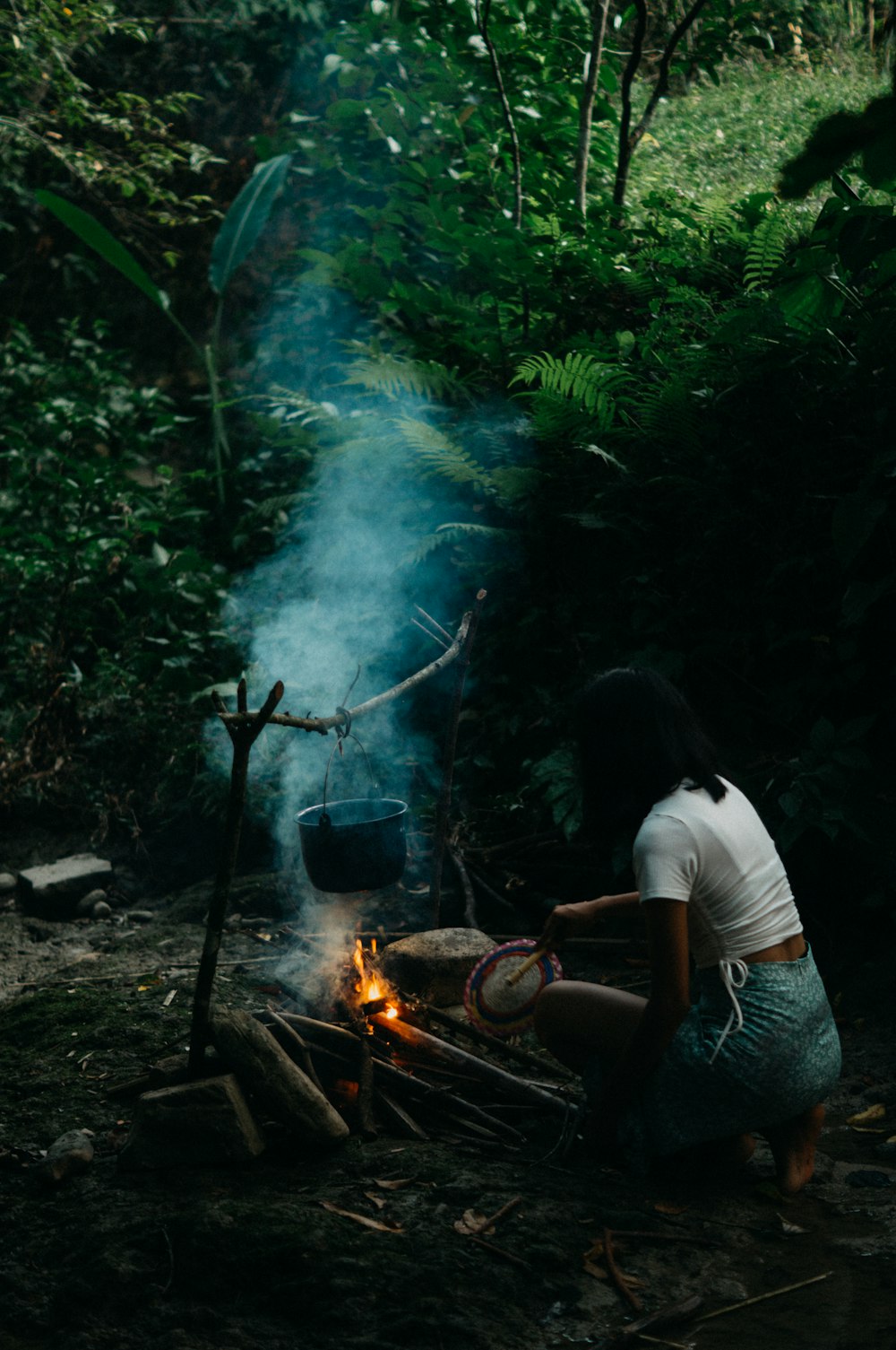 a woman cooking food over a fire in the woods