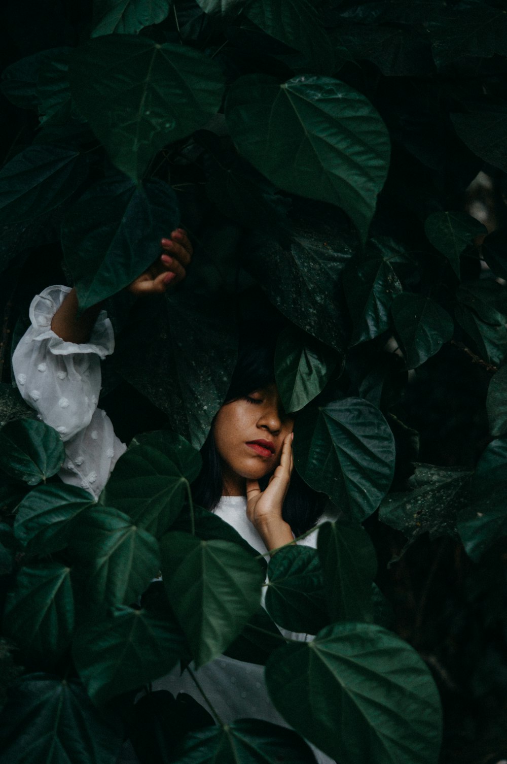 a woman in a white shirt hiding behind a green plant