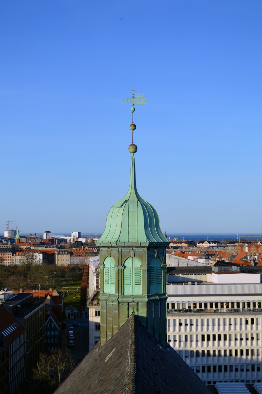 a tall green tower with a weather vane on top of it