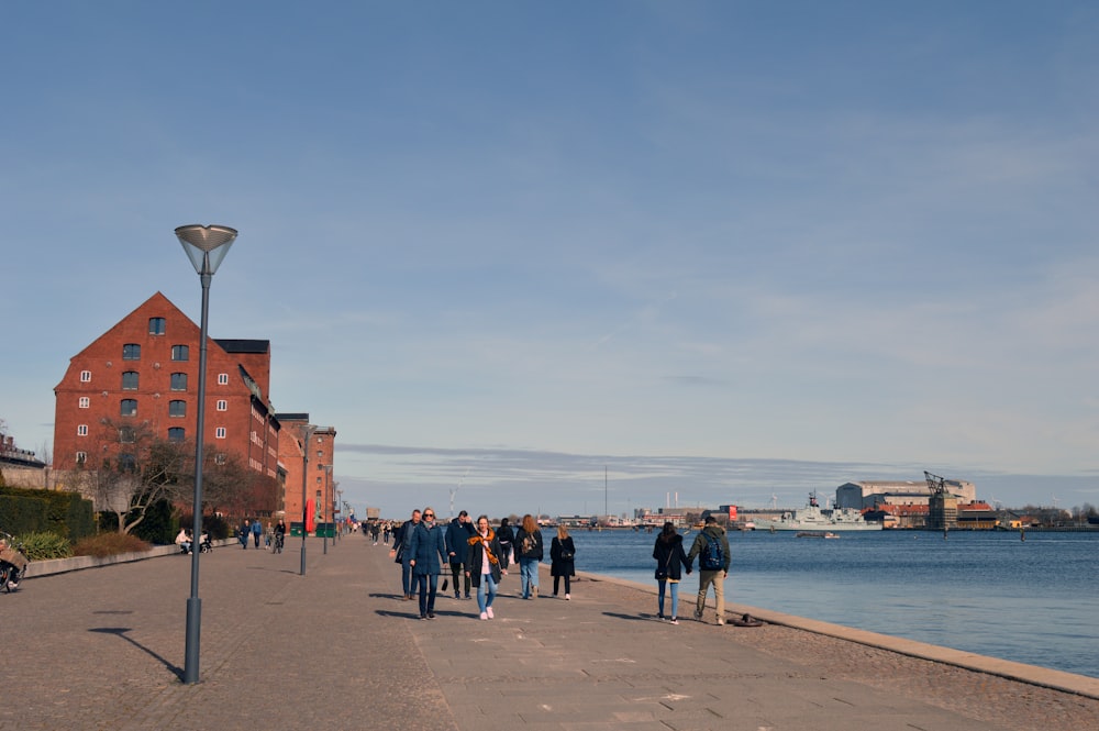 a group of people walking down a sidewalk next to a body of water