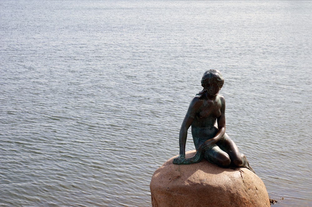uma estátua de uma mulher sentada em cima de uma rocha
