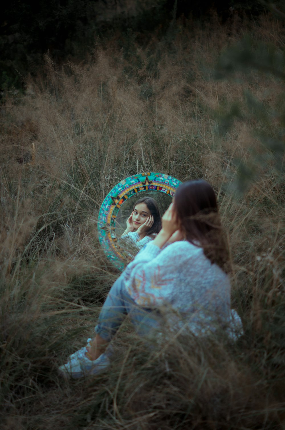 a woman sitting in a field looking at her reflection in a mirror