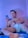 A person is lounging on a bed, holding and looking at a smartphone. The individual wears white underwear and appears relaxed, with a slight smile. The room has a cool blue light ambiance, casting a serene glow.