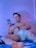 A person is lounging on a bed, holding and looking at a smartphone. The individual wears white underwear and appears relaxed, with a slight smile. The room has a cool blue light ambiance, casting a serene glow.
